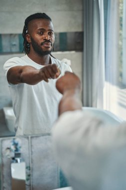 Elinde diş fırçası olan sakin bir adam banyoda duruyor.