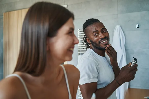 Mężczyzna z promiennym uśmiechem wpatrujący się w kobietę podczas zabiegu golenia — Zdjęcie stockowe