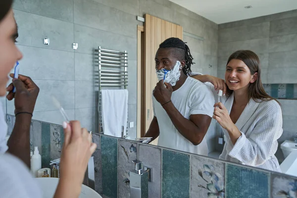 Сосредоточенный мужчина использует свою безопасную бритву перед зеркалом в ванной — стоковое фото