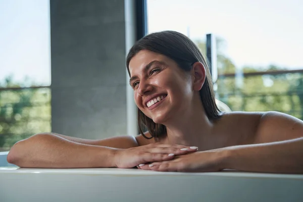 Freudige Frau sitzt in Badewanne und blickt in die Ferne — Stockfoto