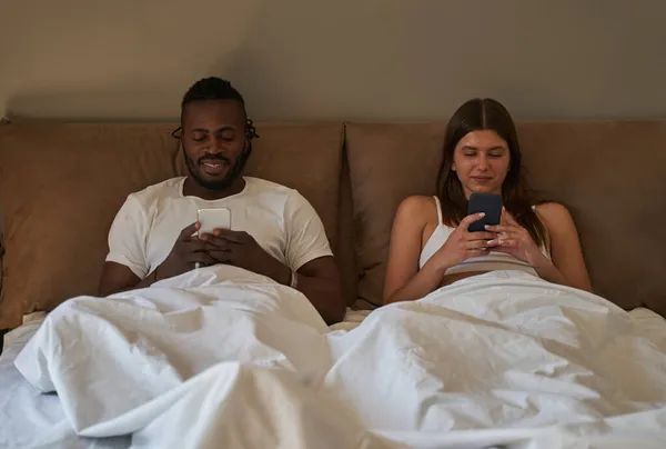 Smiling male and focused female using their cellphones in bedroom — Stock Photo, Image