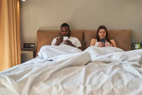 Femeia și bărbatul își folosesc smartphone-urile în dormitor — Fotografie, imagine de stoc