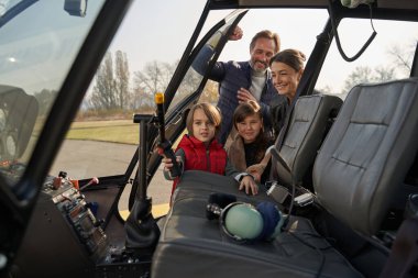 Açık bir helikopter kokpitinin yanında poz veren neşeli bir aile.