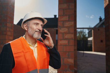 Neşeli inşaat işçisi telefon görüşmesi yapıyor.
