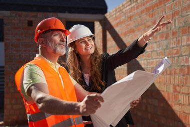 Neşeli kadın mimar ve partneri bina planlarını inceliyor.