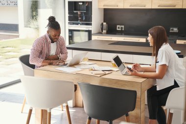 Odaklanmış adamı izleyen bir kadın dizüstü bilgisayarda çalışıyor.