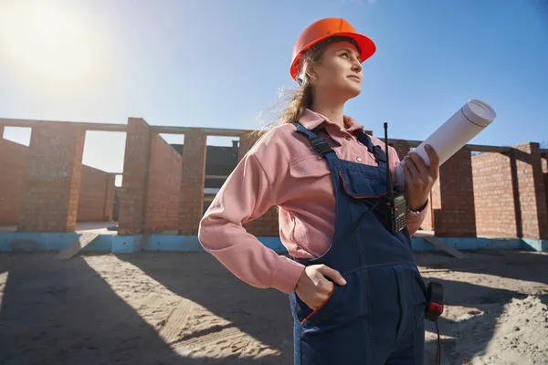 Triumphierende Bauarbeiterin in voller Montur steht in der Nähe eines sonnenbeschienenen Gebäudes — Stockfoto