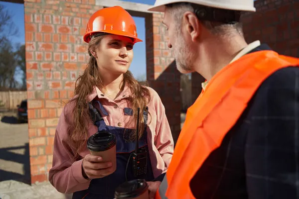 Mujer ambiciosa en hardhat compartir tiempo de café con su compañero de trabajo —  Fotos de Stock