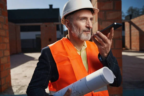 Allvarlig byggare i hårdhatt som har ett samtal på telefon — Stockfoto