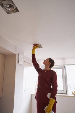 Genç profesyonel temizlikçi kadın tavana asılmış aydınlatmalar.