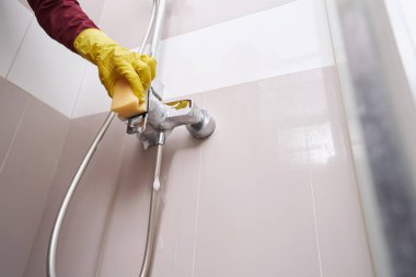 Lastik eldivenli bir işçi banyo musluğunu yıkıyor.