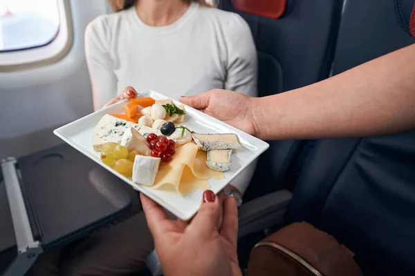 Airline stewardess giving plate with snacks to passenger — Stock Photo, Image