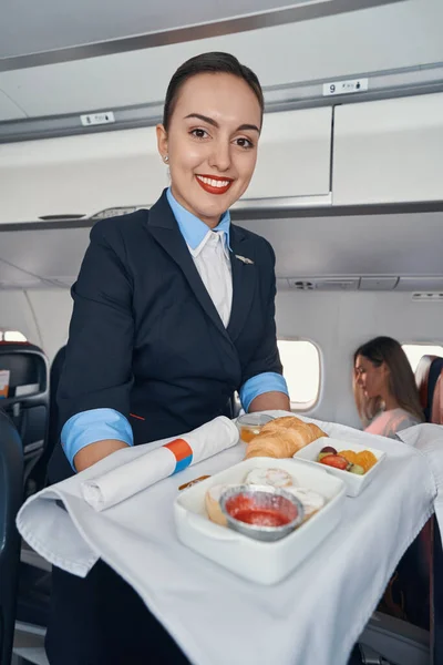Joyful stewardess rolling airline meal trolley through aisle — Stock Photo, Image