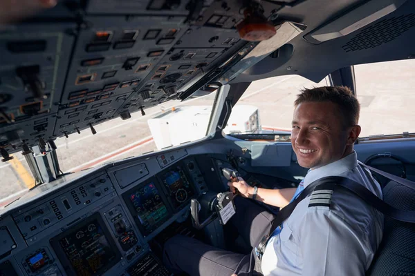 Счастливый пилот самолета улыбается в камеру с рукой на колесе — стоковое фото