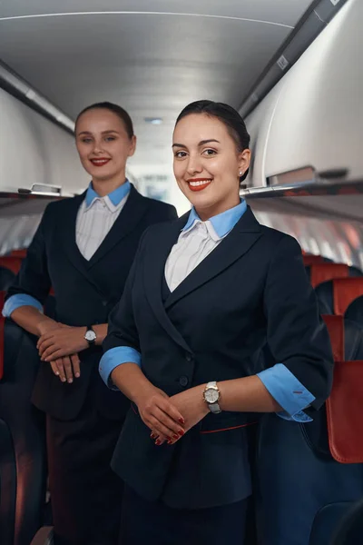 Две стюардессы, стоящие в проходе самолета со сложенными руками — стоковое фото