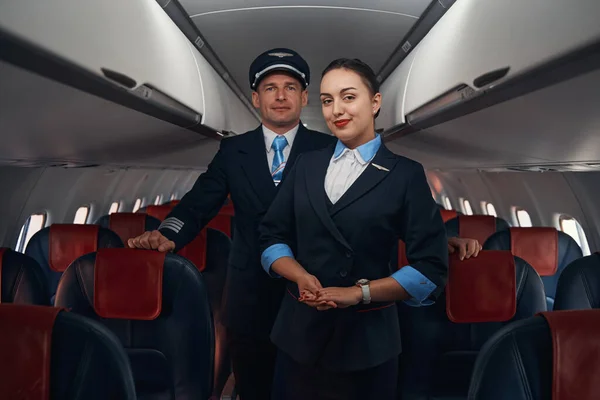 Удовлетворенная стюардесса и пилот, стоящий рядом с пассажирскими сидениями — стоковое фото