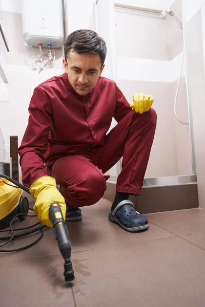 Concentrated janitor steam-cleaning grout line on bathroom floor