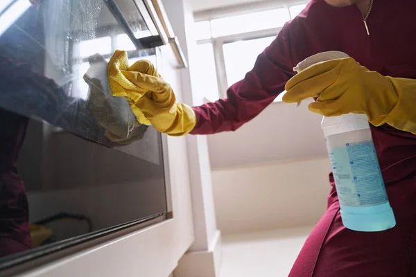 Professional housecleaner in rubber gloves cleaning part of electric cooker