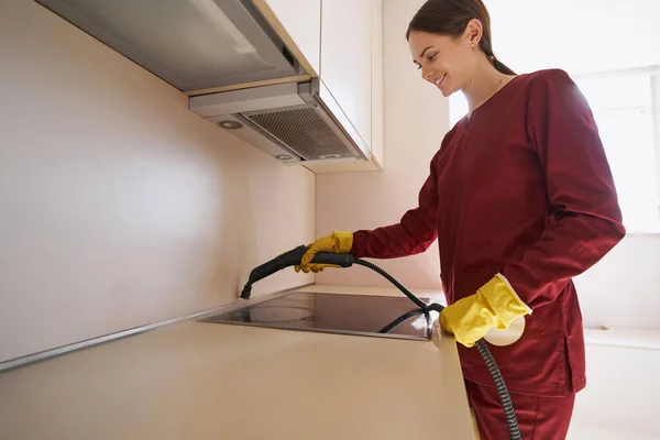 Joyous Kaukasische vrouwelijke conciërge stoom-schoonmaken keuken teller — Stockfoto