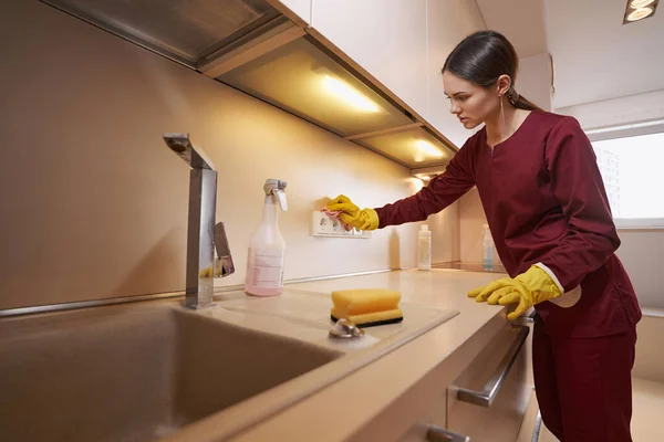 Serious concentrated young Caucasian janitor dusting kitchen