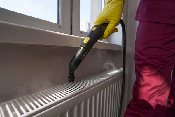 Janitor experiente em radiador doméstico de limpeza a vapor uniforme — Fotografia de Stock