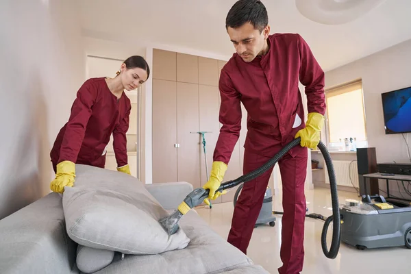 Focused janitorial staff cleaning sofa pillow with steam cleaner