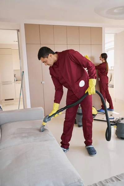 Geschoolde geüniformeerde conciërge schoonmaken woonkamer — Stockfoto