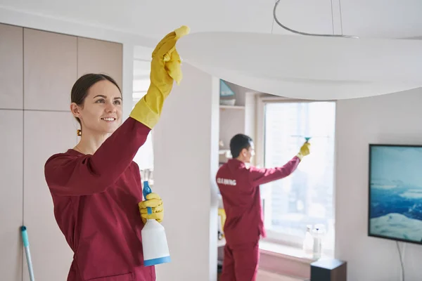 Joyous vrouwelijke reiniger en haar collega schoonmaken woonkamer — Stockfoto