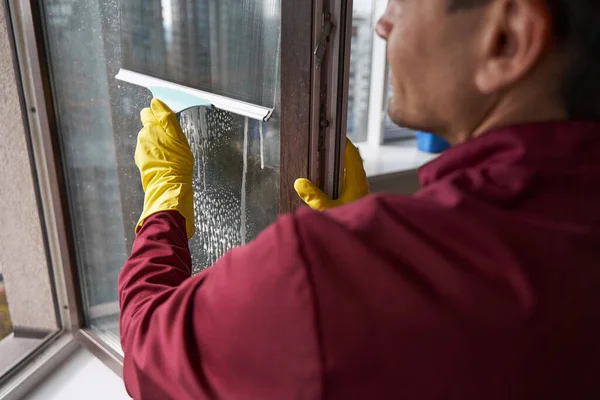 Woźny w gumowych rękawiczkach myje otwarte okno za pomocą squeegee — Zdjęcie stockowe