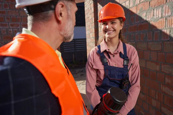 Gladsome senhora em roupa de construtor falando com o homem de chapéu duro — Fotografia de Stock