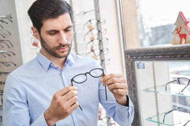 Optik dükkanında gözlüklerin kalitesini değerlendiren adam.