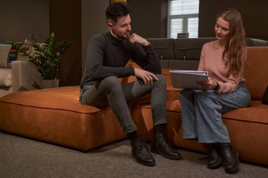 Genç bir kadın, memnun bir adamın huzurunda belge okuyor.