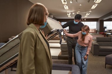 İki alıcı yeni kanepe yatağı seçiyor. Satıcının da yardımıyla.