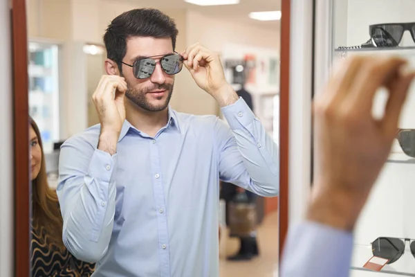 Hombre probándose gafas de sol espejo en tienda óptica — Foto de Stock