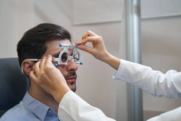 Oční lékař reguluje pozici zkušebního rámu na lidské tváři — Stock fotografie