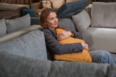 Gülümseyen bayan alışverişçi dükkandaki kanepede hayal kuruyor.