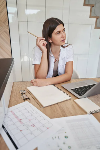 Thoughtful lady seated at wooden desk looking away — Stockfoto