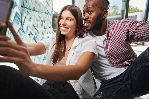 Joyosa pareja de raza mixta tomando selfies en la habitación —  Fotos de Stock