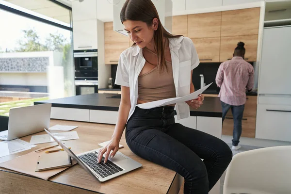 Concentrated woman with documents using her notebook computer — Stockfoto