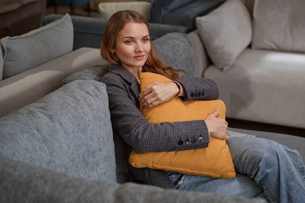 Compradora femenina pensativa sentada en un sofá en una tienda de muebles — Foto de Stock