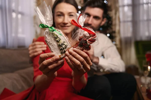 Joyful man and lady holding sweets with Christmas tree on the background — стоковое фото