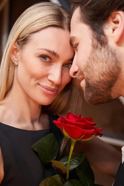 Жінка з трояндою дивиться на камеру поруч зі своїм партнером — стокове фото