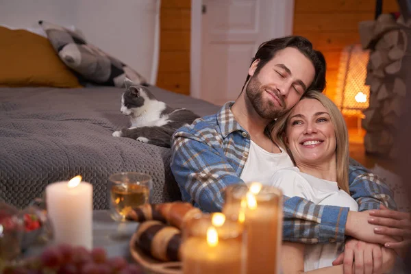 Happy couple hugging on floor near bed with cat — Stockfoto