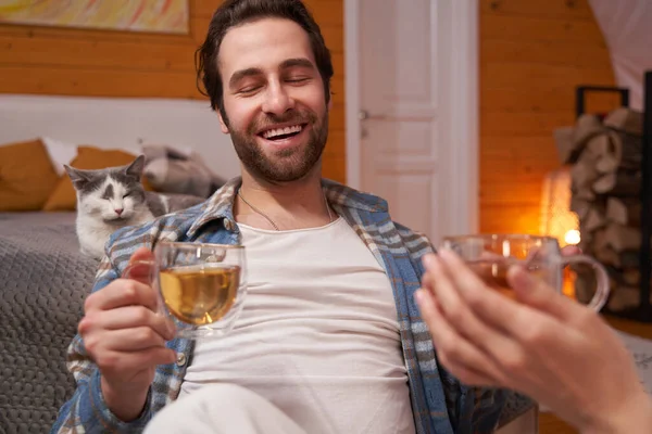 Fröhlicher Mann trinkt Tee im Schlafzimmer neben Katze — Stockfoto