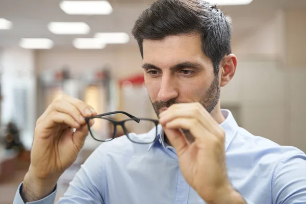 Hombre comprador en la tienda de óptica inspeccionar par de gafas — Foto de Stock