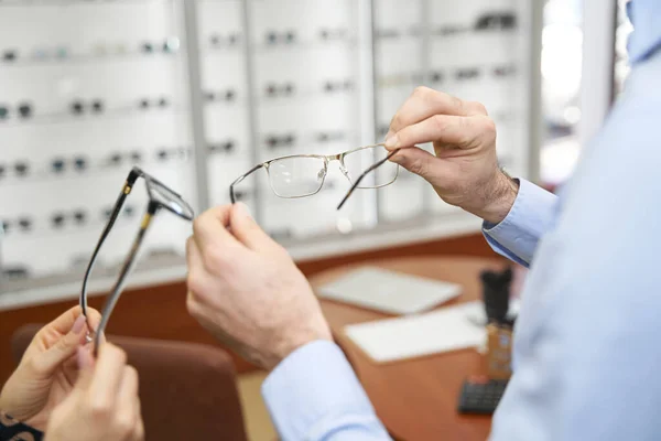 People comparing two eyeglass frames in optical shop — Stockfoto