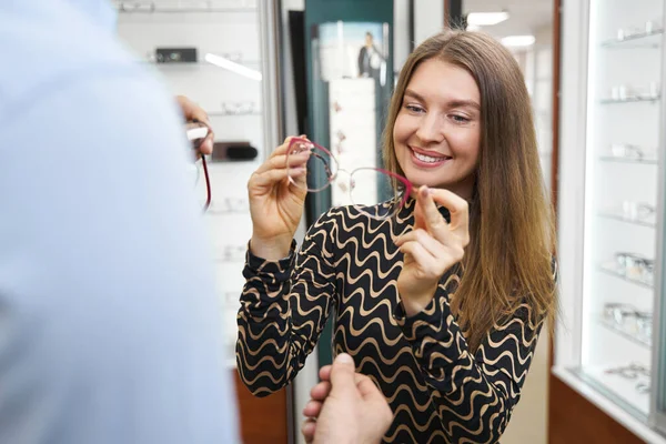 Cheeful woman looking at glasses with red frame — Fotografia de Stock