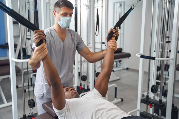 Mužský pacient cvičí na tělocvičně pod dohledem fyzioterapeuta — Stock fotografie