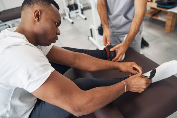 Man sätter vikter på sina vrister assisterad av sjukgymnast — Stockfoto