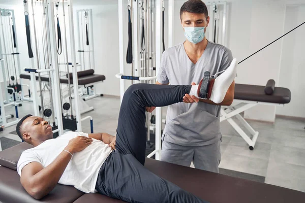 Hombre realizando ejercicio de piernas asistido por fisiatra certificado —  Fotos de Stock